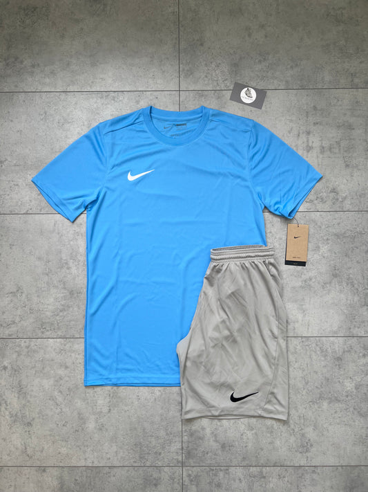Flat-lay of Nike Dri Fit outfit set featuring a University Blue slim-fit t-shirt with light grey shorts, both with tags attached, laid out on a grey tiled background.