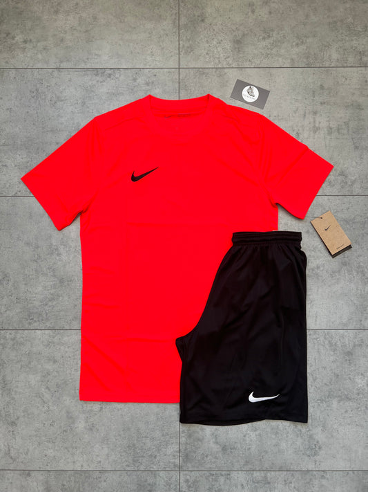 Flat-lay of Nike Dri Fit set featuring a bold bright crimson slim-fit t-shirt and black shorts with tags, displayed on a tiled surface.