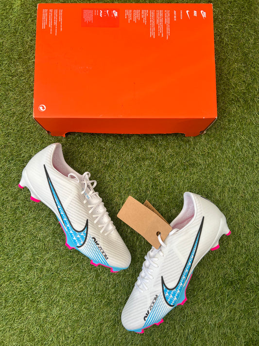 Nike Air Zoom Mercurial Vapor 15 Academy FG/MG football boots in white, Baltic Blue, and Hot Punch – lightweight synthetic upper with bold pink Swoosh and blue soleplate. Displayed on grass background, available at Sneaker Dyl.