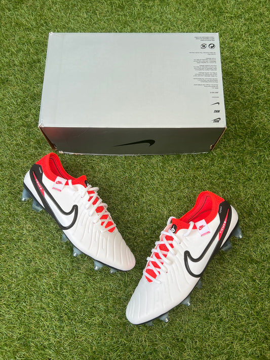 Nike Tiempo Legend 10 Elite SG-PRO AC football boots in white, black, and bright crimson – soft white upper with red studs, black Swoosh, and Anti-Clog soleplate for soft ground. Shown with accessories on grass. Available at Sneaker Dyl.
